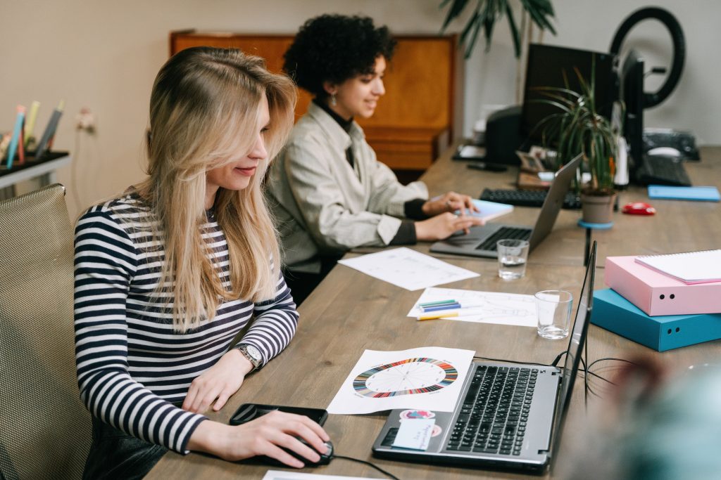 Two women collaborating at their laptops in a modern office setting, fostering teamwork and creativity.